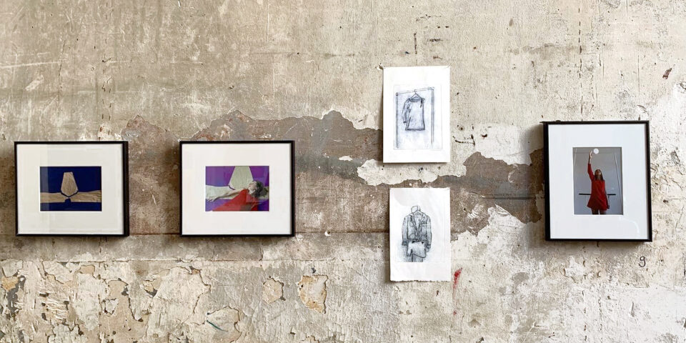 Three framed photos and two smaller sketches are hung on a textured concrete wall. The frames are black and the images inside and surrounded by a white border. The photos show a woman in a red dress amongst various backgrounds. The sketches are in pencil and offer two different torsos of a body.