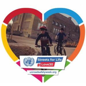 An image of two young boys riding on bikes with helmets is seen inside of a heart. The heart has a colourful border around it, the colours are red, blue, orange, green, pink, and yellow, and there is a white banner at the bottom that says "Streets for Life #Love10" and a website link.