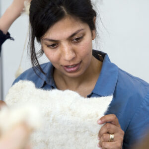 Dark haired woman wearing a light blue shirt inspects a piece of white felt in her hands.